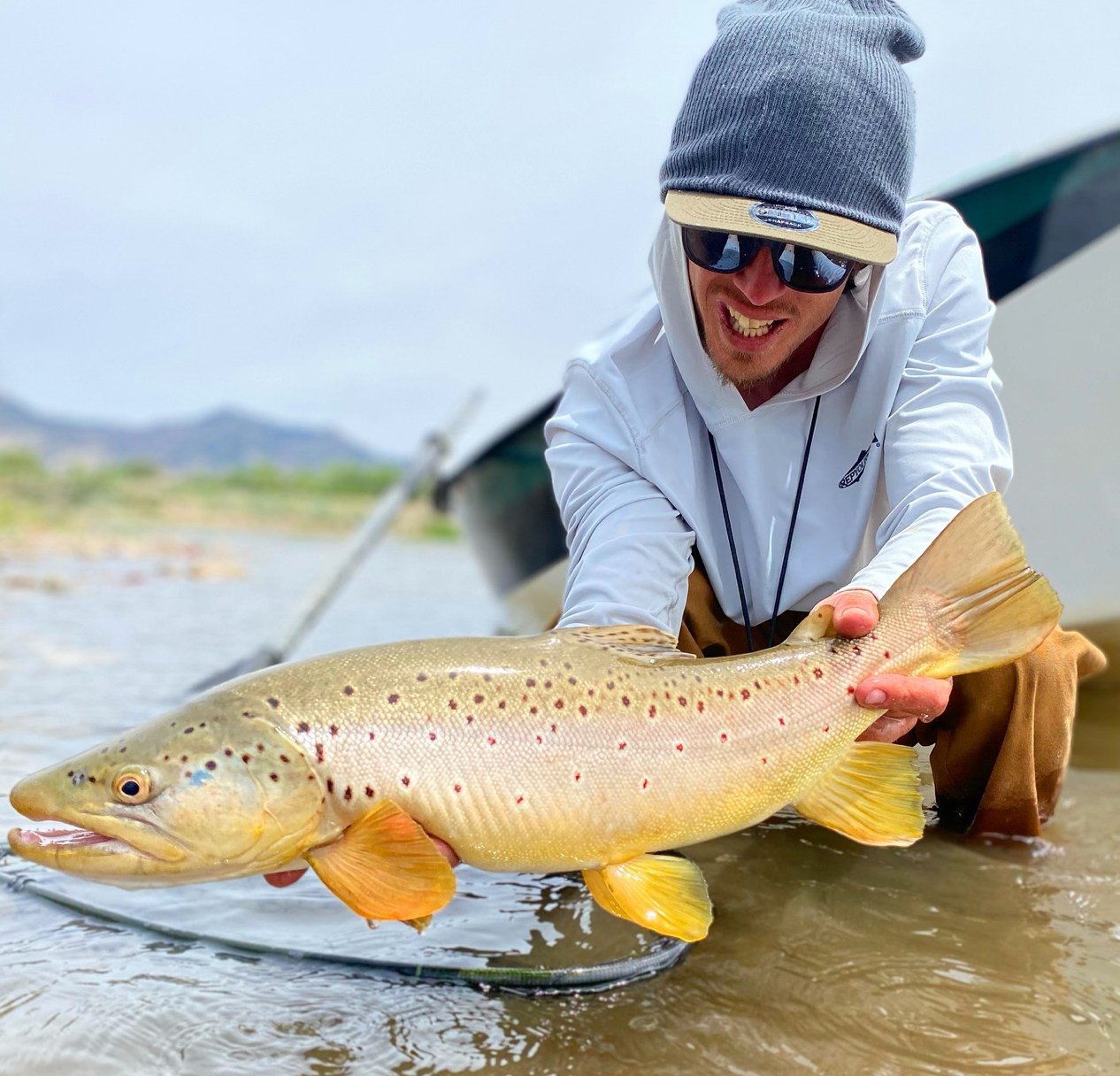 Person holding a large fish in a body of water with mountains in the background