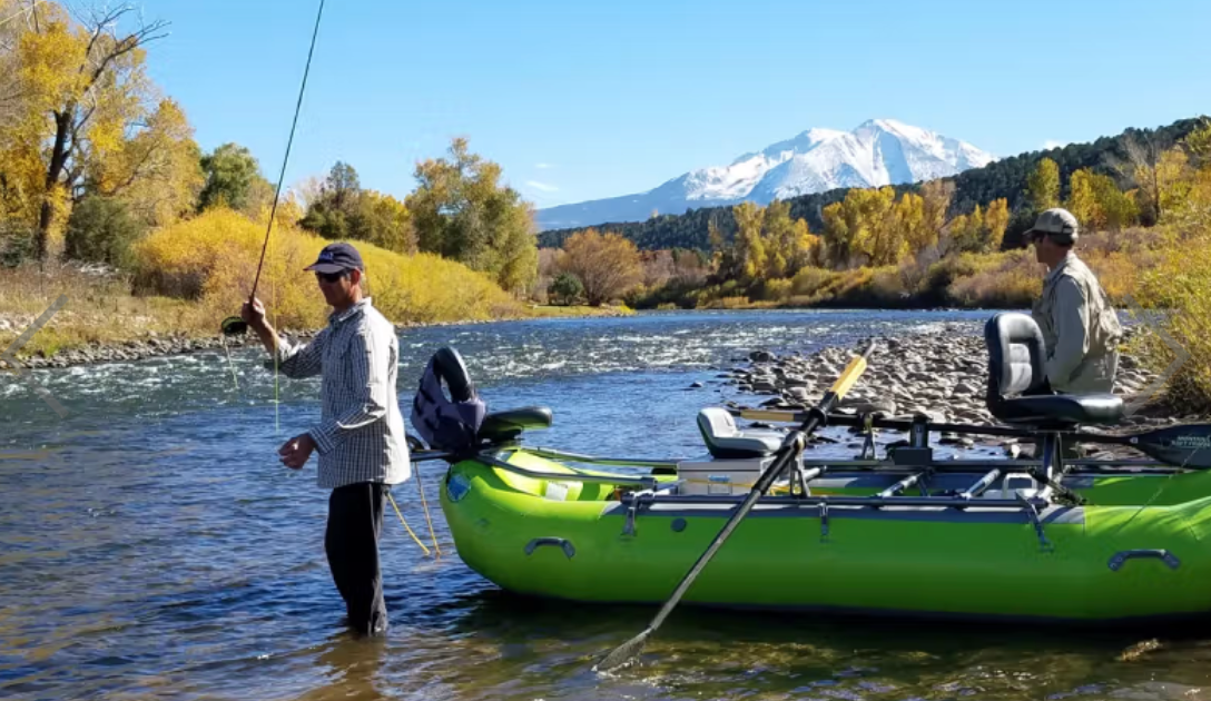 Two people with kayaks on a river with mountains in the background